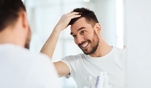 Patient in Hays smiling in mirror after dental implant care routine