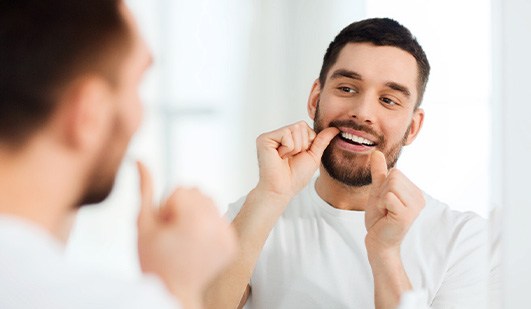 Man in white shirt flossing teeth