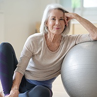 Senior woman smiling while resting against balance ball