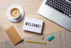 An index card that says “welcome” sitting on a desk next to a cup of coffee and a laptop